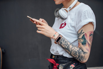 Close-up of tattooed young woman with headphones using cell phone