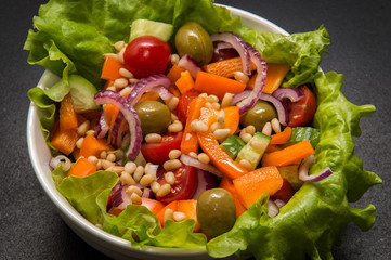 Close up, macro. Vegetarian food. Bowl of vegetable salad with tofu and pine nuts. Black background.