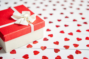 Valentine's Day decoration composition. Boxed gift placed on heart shaped red sequins on white wooden table. Romantic background. Flat lay, top view.