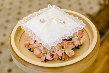 A pair of wedding rings on a white pillow, the edges of which are decorated with lace. The pillow is on the flowers.