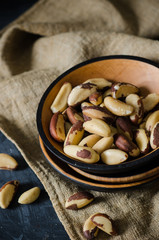 Tasty brasil nuts in a wood plate on linen napkin on black background