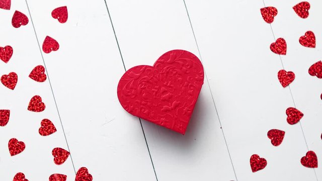 Valentine's Day decoration composition. Heart shaped red sequins placed on white wooden table. Frame with copy space with heart in the middle. Romantic background. Flat lay, top view.