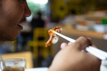 Man use chopsticks eating boiled slice pork from shabu or Sukiyaki hot pot.
