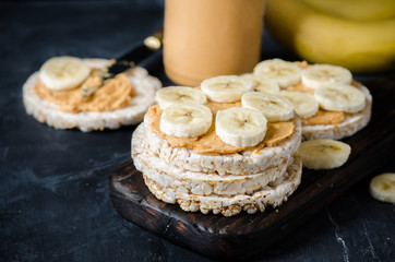Rice cakes with peanut butter and slices of banana on black wooden table. Space for text