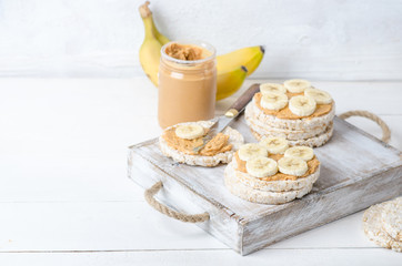 Healthy breakfast with rice cakes with peanut butter and slices of banana on white wooden table. Space for text.