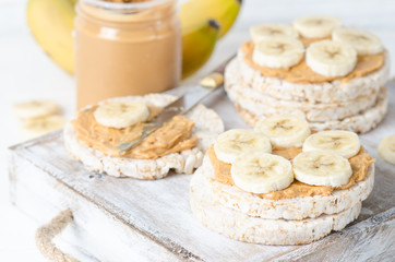 Healthy breakfast with rice cakes with peanut butter and slices of banana on white wooden table