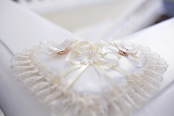 A pair of wedding rings on a white heart-shaped pillow. Along the perimeter of the pillow is a lace fabric