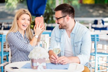 Happy young woman is surprised after receiving a gift box from her boyfriend. Enjoying romantic moments in a cafe