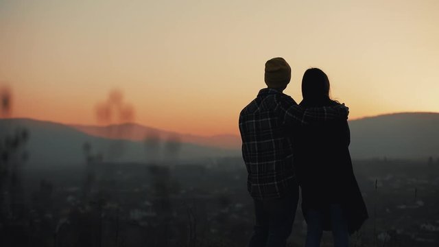Silhouette of young couple in love enjoying a sunset over the mountains. Vacation, travel, romance, marriage proposal concept