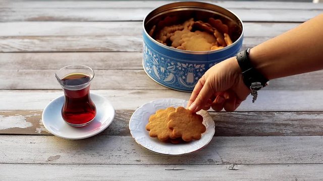 Woman serving cookies with turkish tea on the wooden table.