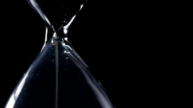 The sand flow in the hourglass with black background and lateral light backlight in lateral composition and possible endless loop
