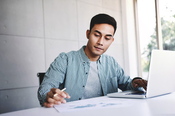 Happy Young Asian Businessman Working on Computer Laptop in his Workplace