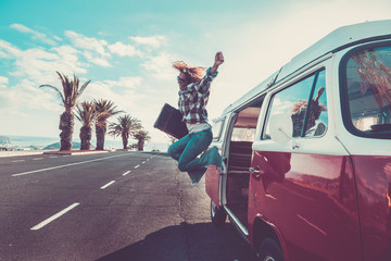Happiness for travel and enjoying wanderlust concept for beautiful curly crazy woman jumping out the old van with vintage luggage - joyful and success lifestyle for alternative hipster people - obrazy, fototapety, plakaty