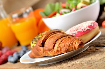 Donuts and croissant, orange juice and fresh salad - breakfast on wooden table