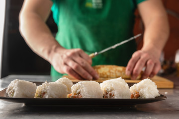 a knife in his hand cuts a roll of rice. closeup on a wooden board