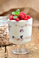 Greek yoghurt with oatmeal and fresh raspberries in a glass and mint leaves - vertical photo