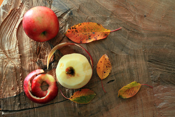 Autumn fruits from the home garden. Two apples - one peeled, and yellowed leaves on a wooden board. Food, healthy, vitamin, natural.