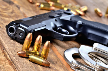 9mm pistol handgun, special police hollow-point expanding bullets and handcuffs on old wooden table - view to the barrel