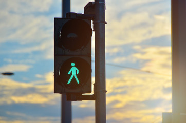 Green semaphore pedestrian light close-up. Sunset in background.