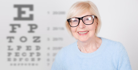 Senior woman in glasses having eye on the vision testing tables background. Visiting a doctor...