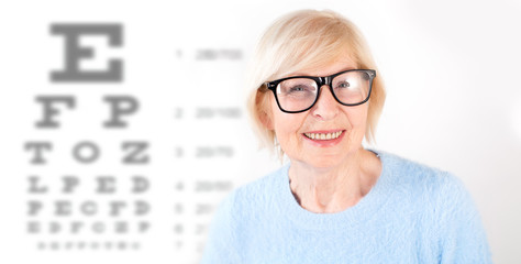 Portrait of senior woman in glasses, having eye on the vision testing tables background. Visiting a...