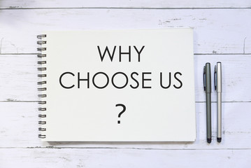 Top view of pen and notebook written with question Why choose us? on white wooden background.