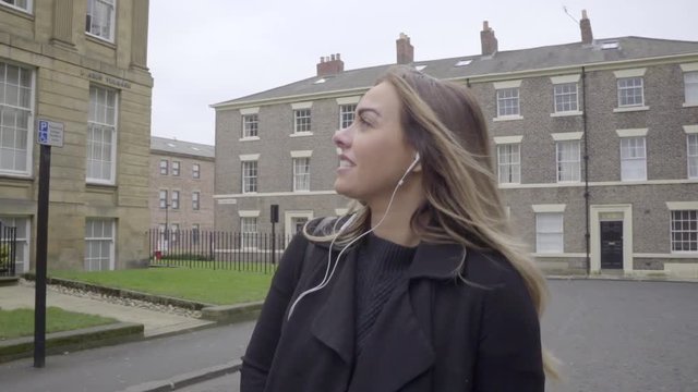 happy woman listening to music on headphones in front of old buildings