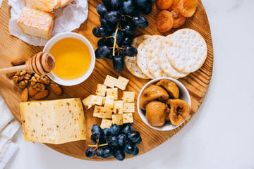 Flat lay with various types of cheese, grapes, nuts, honey and cracker in wooden board on marble