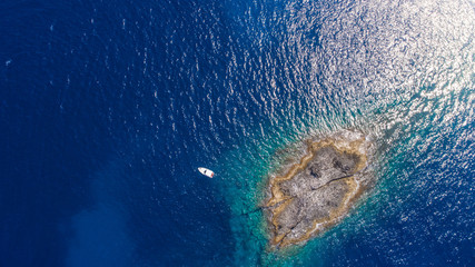 Aerial top view of a deserted island with white boat. Rocky shore of Zannone island near Ponza, Italy. Blue clear water on sunny day.
