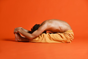 old man practices Ashtanga Vinyasa yoga back bending asana Paschimottanasana - seated forward bend