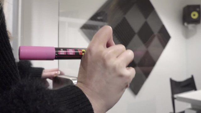 womans hand writes the word marketing on glass in office