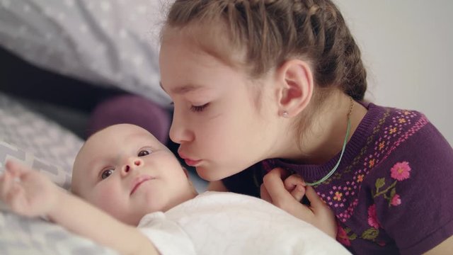 Beautiful girl kissing baby lying on sofa. Sister kiss newborn brother