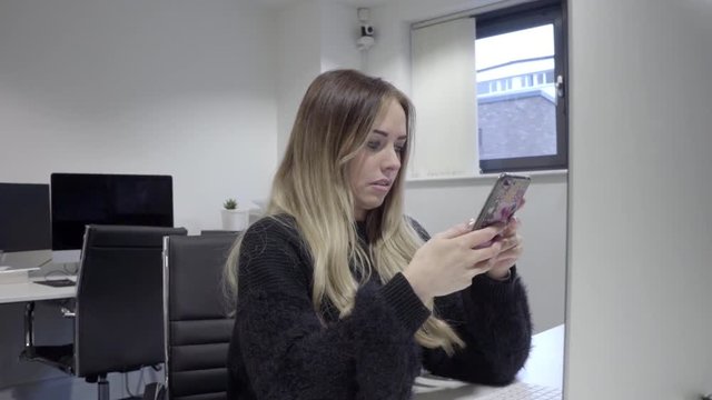 woman at desk using social media on phone at work