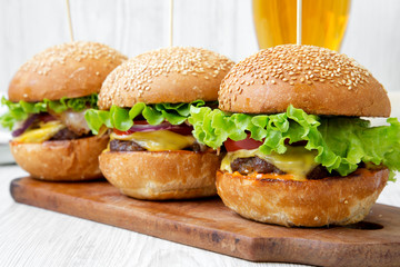 Homemade cheeseburgers on rustic wooden board and glass of cold beer, side view. Close-up.