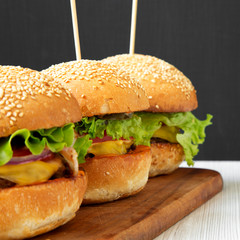 Homemade cheeseburgers on wooden board, side view. Close-up.