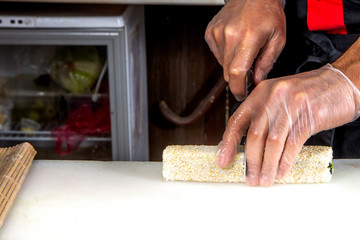 closeup of chef hands rolling up sushi cuts into portions on kitchen