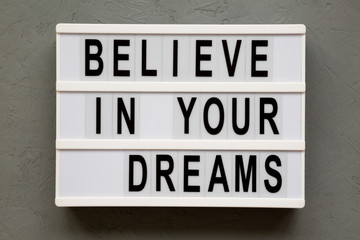 Lightbox with text 'Believe in your dreams' over concrete background, top view. From above, overhead, flat lay.