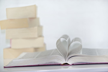 Heart shape from paper book against white background and pile of books