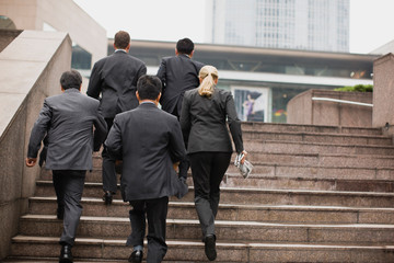 Group of businesspeople walking up a flight of stairs outside a building in the city.