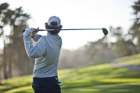 Man swinging a golf club over his shoulder while playing golf on a golf course.