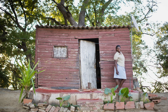 Portrait of a mid-adult woman standing outside a shanty house.