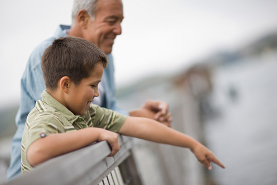 Boy pointing over a railing while standing next to his father on a wharf.