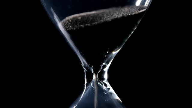 The sand flow in the hourglass with black background and lateral light backlight in centered composition