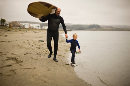Father and son with surfboard walking on beach