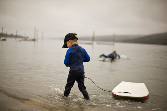 Little boy in wetsuit playing with body board.