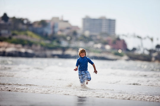 Young boy dressed in blue,  splashing in the ocean.