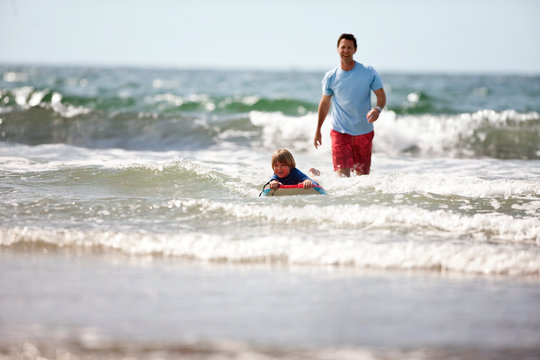 Father teaching young son how to ride a wave on a boogie board.
