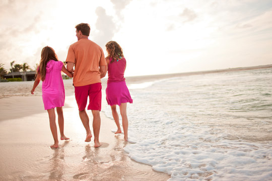 Mid-adult man walking hand in hand with his two daughters along a remote sandy beach.