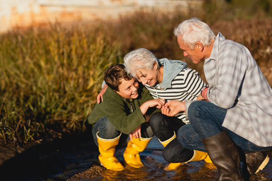 Boy and his grandparents smile and talk as they crouch together on a sodden path.