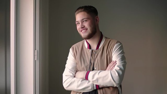 Smiling young Caucasian man posing at camera with arms crossed. Portrait of happy cheerful hipster guy with trendy haircut, wearing casual jacket and t-shirt. Video portrait concept